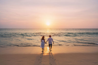 Couple on beach against sky during sunset