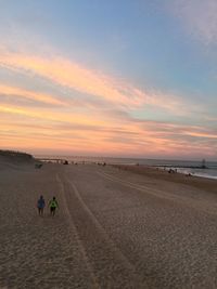 People on sand dune against sky during sunset