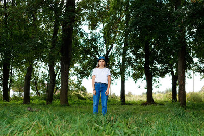 Overall portrait of a serious young woman with brown hair wearing a hat outdoors. green nature trees 