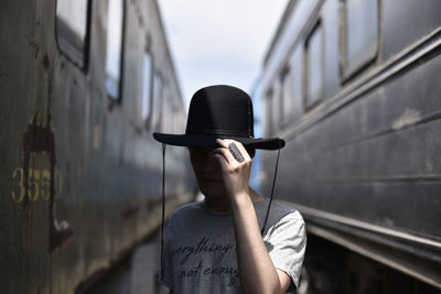 Portrait of man holding hat while standing on railroad track
