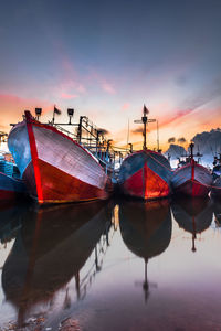 Boats moored at harbor against sky during sunset