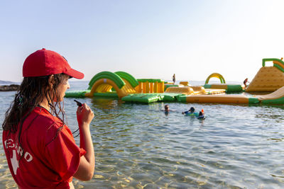 Lifeguard on rescue duty, standing on shore with whistle and looking to the aquapark