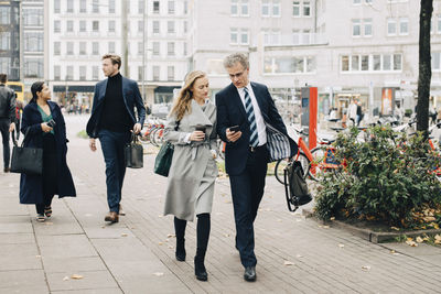 Businessman showing smart phone to female colleague while walking in city