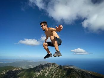 Full length of woman jumping on mountain against sky