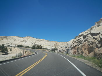 Road leading towards mountains against clear blue sky