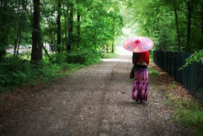 Rear view of woman walking on road in forest