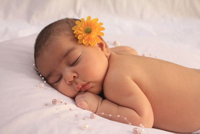 Close-up of baby girl with flowers on bed