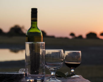 Close-up of glasses and wine bottle on table against sky during sunset