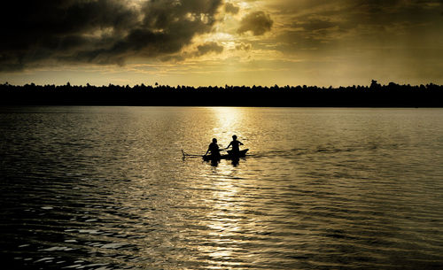 Silhouette people in lake against sky during sunset