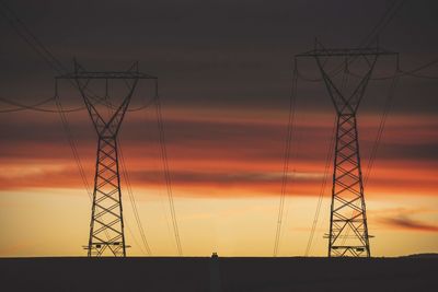 Low angle view of silhouette electricity pylon against sky at sunset