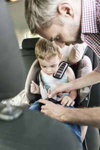 Father fastening seat belt for son in car