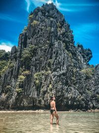 Woman standing in sea by rock formation against sky