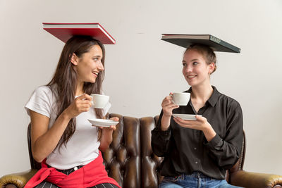 Young women holding coffee cups with books on head