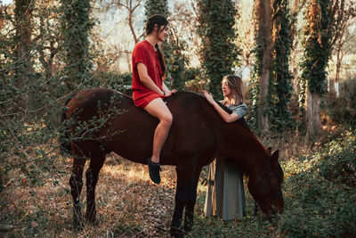 Woman sitting on horse with friend standing in forest