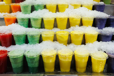Iced fruit smoothies in the flavors of banana, grapefruit, orange, kiwi, inside plastic glasses.