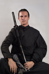 Portrait of serious samurai with katana sitting against gray background