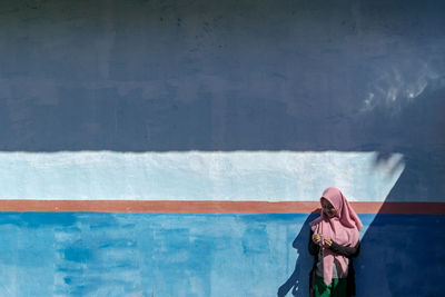 Teenage girl wearing hijab while standing against wall