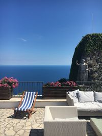 Chairs and sofa on building terrace against sea during sunny day