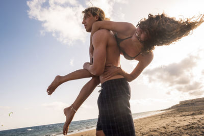 Man carrying woman over shoulder at the beach against sky