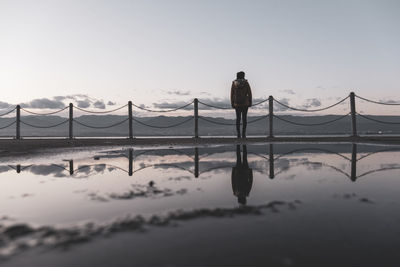 Rear view of silhouette man standing on bridge against sky