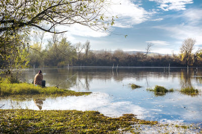 Rear view of man by lake against sky