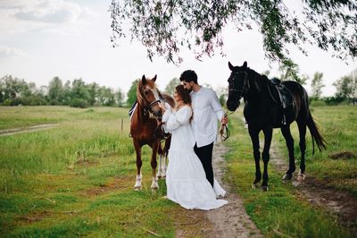 Wedding couple standing with horses on field