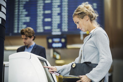 Side view of businesswoman using check in machine at airport