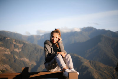 Woman sitting on mountain against sky