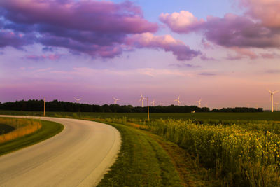 Road passing through field against cloudy sky