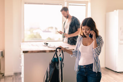 Woman with luggage talking on smart phone while man standing in background at apartment