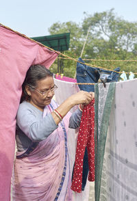 Portrait of a simple looking mature indian woman hanging freshly washed laundry to dry in the sun