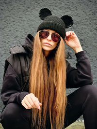 Portrait of young woman wearing sunglasses while standing against wall