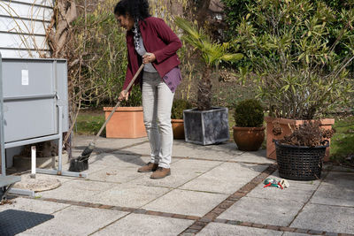 Full length of woman cleaning with broom while standing on footpath in yard