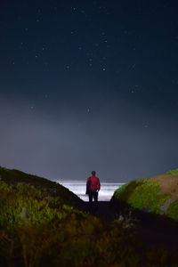 Rear view of man standing on field against sky at night