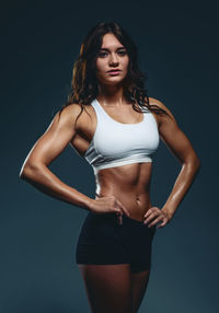 Portrait of young female athlete standing against blue background