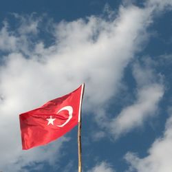 Low angle view of turkish flag waving against cloudy sky