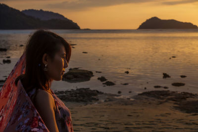 Woman looking away while standing at beach during sunset