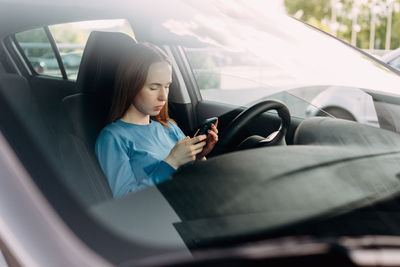 Young woman using mobile phone in car