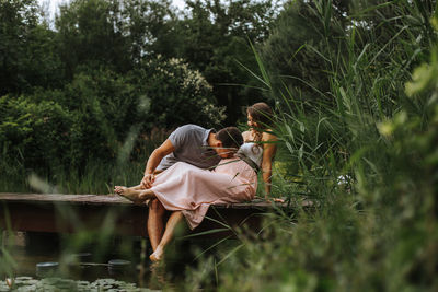 Man kissing pregnant girlfriend on footbridge over lake at park