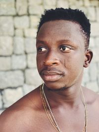 Close-up of shirtless man looking away standing by wall