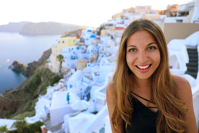 Portrait of smiling young woman against buildings by sea
