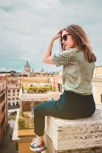 A young woman sits with her back on a rooftop with a panoramic view of rome, italy.