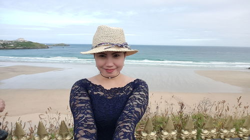 Portrait of young woman standing at beach against sky