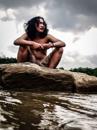Young man sitting in water against sky
