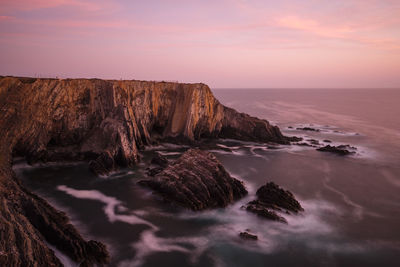 Rock formation in sea against sky during sunset