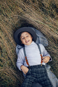 Boy child in plaid pants, hat, suspenders and scarf stands in a field in autumn