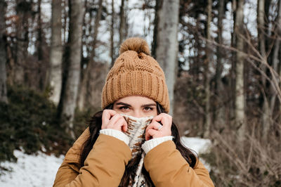 Portrait of young woman holding scarf over her face. winter, outdoors, warm clothes.