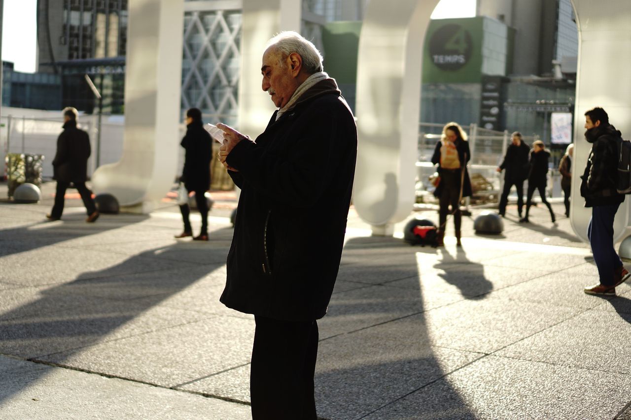 sunlight, walking, shadow, architecture, real people, building exterior, city, incidental people, built structure, outdoors, day, men, lifestyles, full length, one person, people, adult