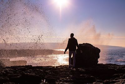 Silhouette of man with arms raised against sunset sky