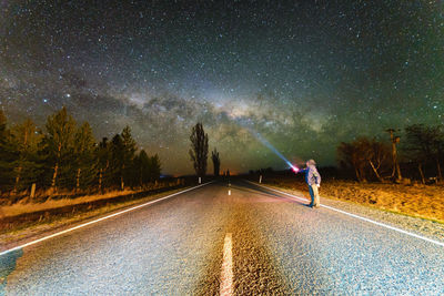 Man holding flashlight against star field on road